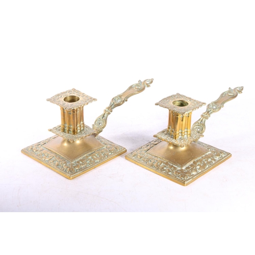 66 - Pair of brass chamberstick candlesticks with dolphin and floral decoration, raised on square bases w... 