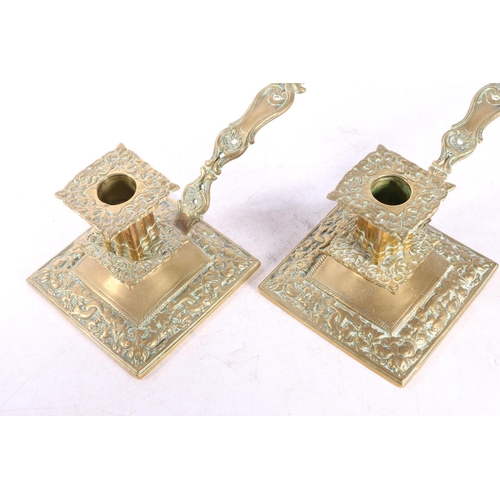 66 - Pair of brass chamberstick candlesticks with dolphin and floral decoration, raised on square bases w... 