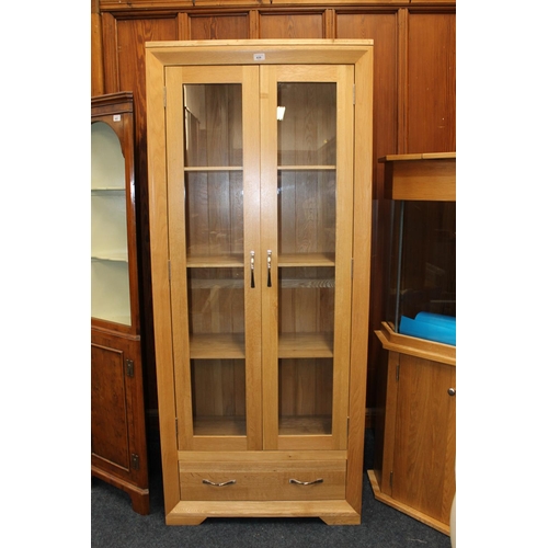 439 - Modern solid wood display cabinet with two glazed panel cupboard doors and baser drawer, 184cm tall.