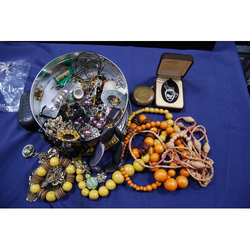 247 - Tin containing costume jewellery to include wooden beads, chains, pendants and a pocket watch case.