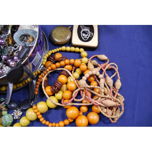 247 - Tin containing costume jewellery to include wooden beads, chains, pendants and a pocket watch case.