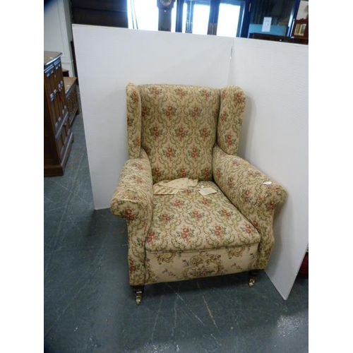 287 - Antique upholstered wing armchair on later brass castors.