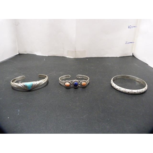 241 - Two silver bangles, one set with lapis-style and coral-style stones, 44.4g gross, and another bangle... 