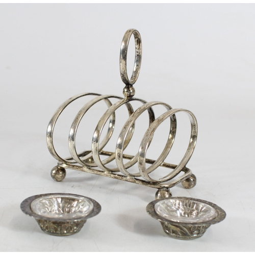 567 - Pair of Indian white metal salts with glass liners, W5cm, together with a silver plated toastrack.