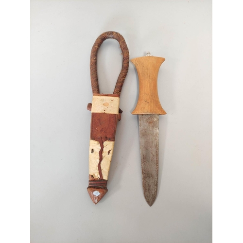 346 - A Sudanese arm knife with tapering straight blade and carved wooden hilt. Contained in tooled leathe... 