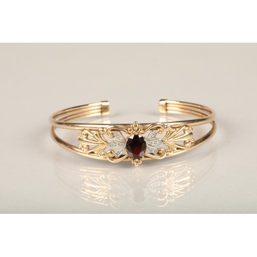 222 - 9ct gold and garnet set bangle, the central oval cut garnet flanked by illusion set diamonds on a ba... 