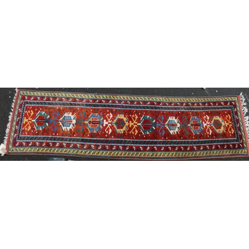 627 - Turkish wool runner, the geometric motifs on red ground within polychrome borders, 298cm x 82cm.