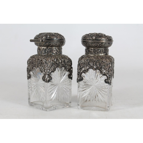 550 - Pair of Victorian cut glass toilet bottles with silver covers and mounts decorated with repoussé cla... 