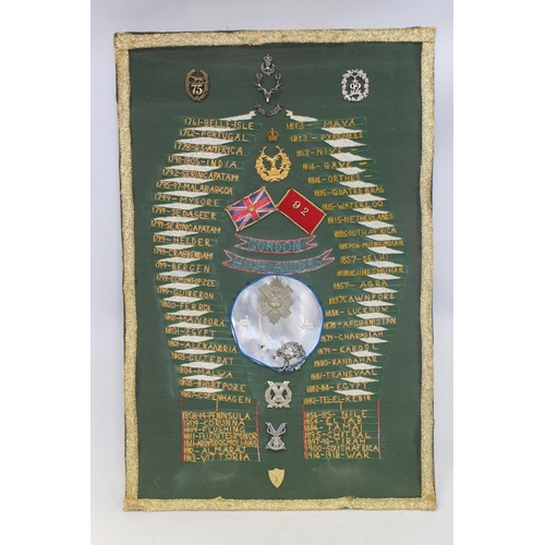 674 - Framed board of The Gordon Highlanders interest with central helmet plate and cap badges within a ne... 