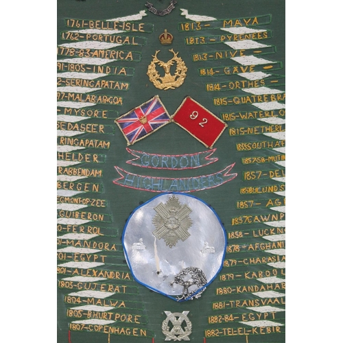 674 - Framed board of The Gordon Highlanders interest with central helmet plate and cap badges within a ne... 