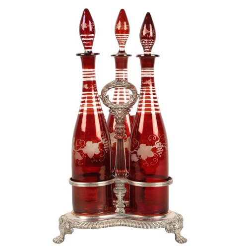 Epns tantalus with central carrying handle fitted three Cranberry glass decanters and stoppers.