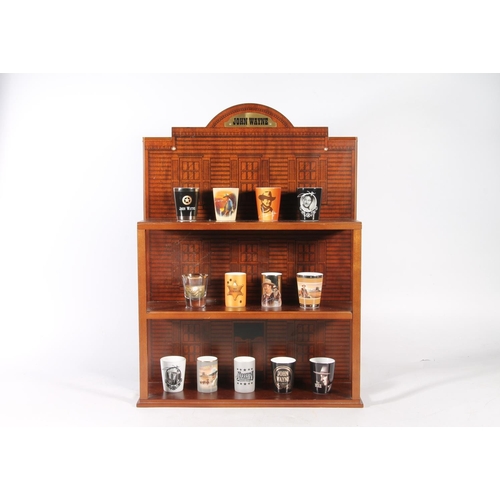 66 - Thirteen John Wayne themed shot glasses, on wall mountable stand.