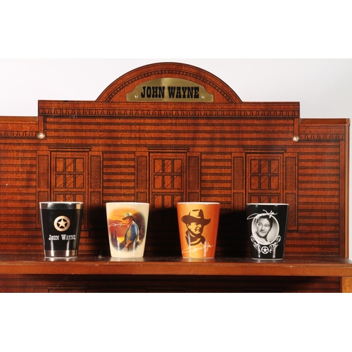 66 - Thirteen John Wayne themed shot glasses, on wall mountable stand.