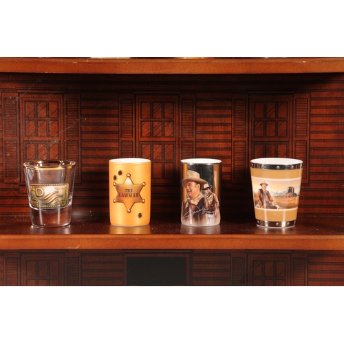 66 - Thirteen John Wayne themed shot glasses, on wall mountable stand.