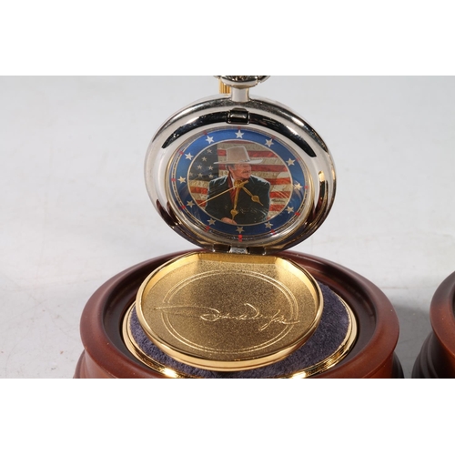 75 - Two John Wayne pocket watches, in glass domed watch holders, 14cm high.