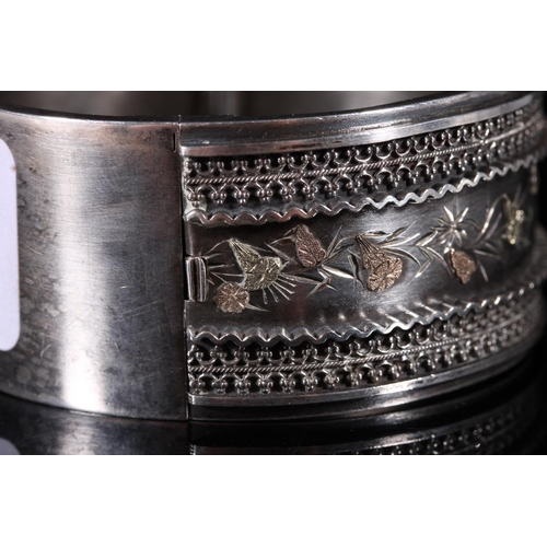 185 - Victorian silver hinged bangle with two tone embossed gold floral decoration between an applied wire... 