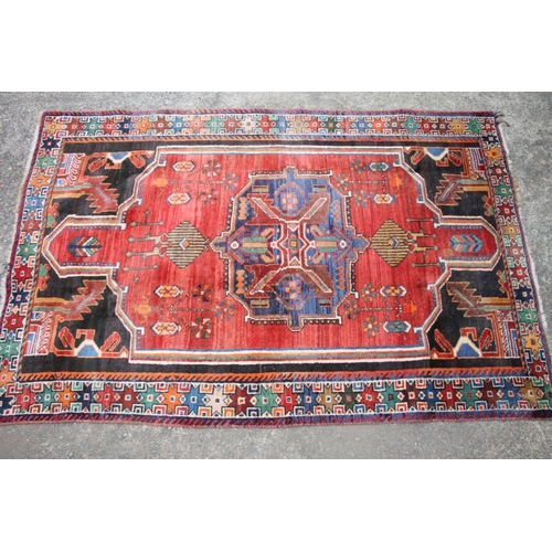 419 - Persian Shiraz region rug, the central blue geometric medallion on a red ground, bordered with black... 