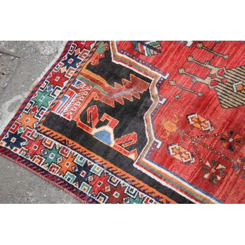 419 - Persian Shiraz region rug, the central blue geometric medallion on a red ground, bordered with black... 