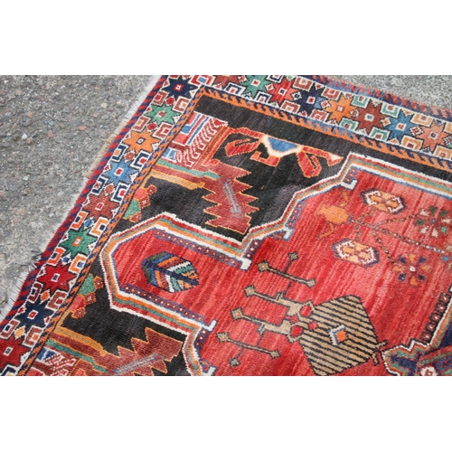 419 - Persian Shiraz region rug, the central blue geometric medallion on a red ground, bordered with black... 