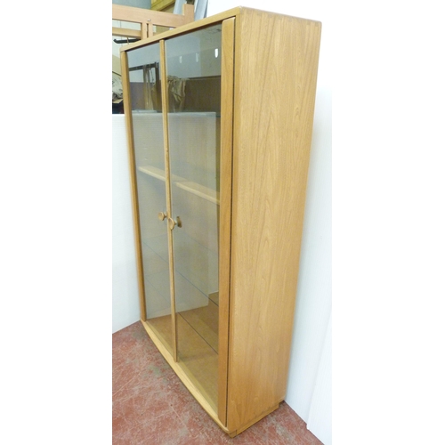 507 - Ercol beech and elm display cabinet, with twin glazed doors enclosing wooden and glass shelves, the ... 