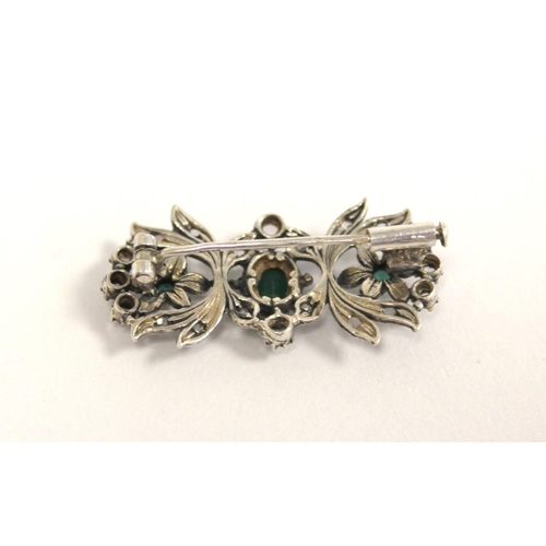 94 - Continental silver floral brooch with three collet set emeralds surrounded by old cut diamonds.