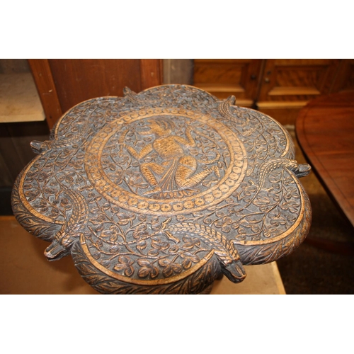 699 - Indian teak occasional small table, the shaped top carved with a foliate field around a mythological... 