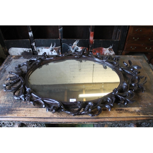 643 - Black Forest style wall mirror, carved with foliate branches, 109cm high.