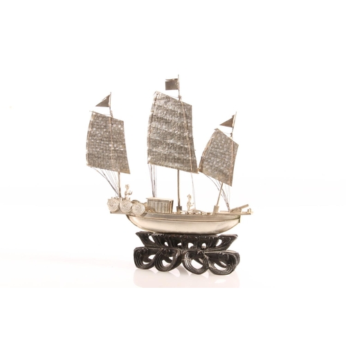 125 - Oriental white metal model of a triple masted sailing boat or junk, raised on carved wooden stand, 6... 