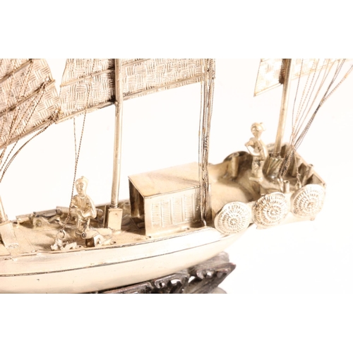 125 - Oriental white metal model of a triple masted sailing boat or junk, raised on carved wooden stand, 6... 