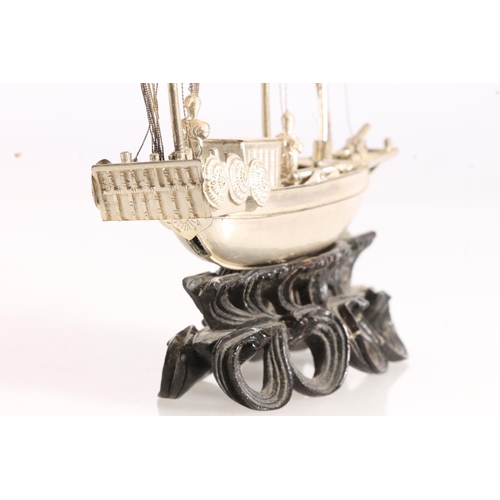 125 - Oriental white metal model of a triple masted sailing boat or junk, raised on carved wooden stand, 6... 