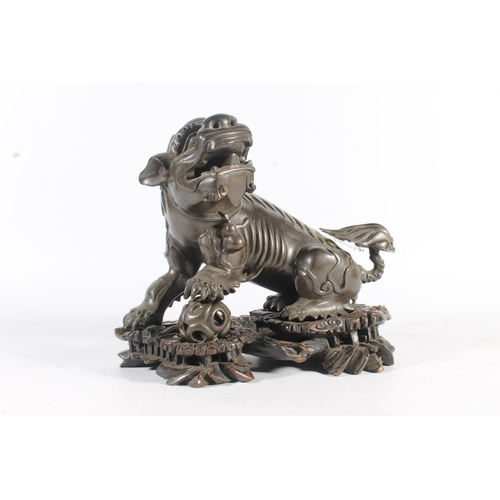 486 - Chinese cast bronze temple dog modelled resting paw on orb, raised on carved wood base, 26cm tall.