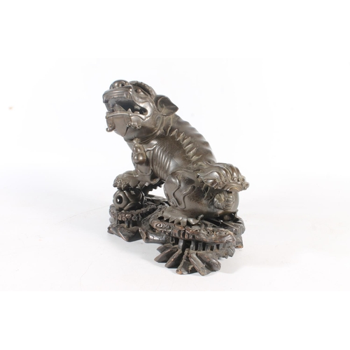 486 - Chinese cast bronze temple dog modelled resting paw on orb, raised on carved wood base, 26cm tall.