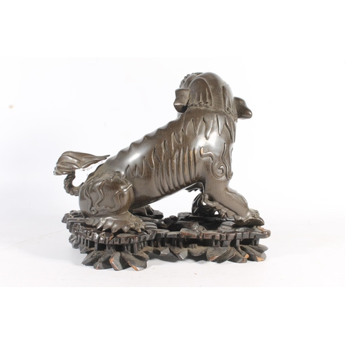 486 - Chinese cast bronze temple dog modelled resting paw on orb, raised on carved wood base, 26cm tall.