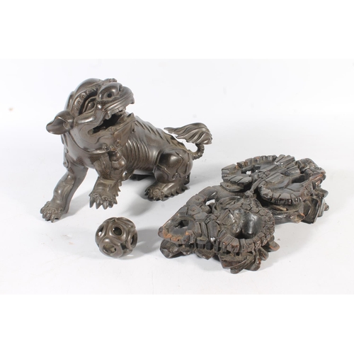 486 - Chinese cast bronze temple dog modelled resting paw on orb, raised on carved wood base, 26cm tall.