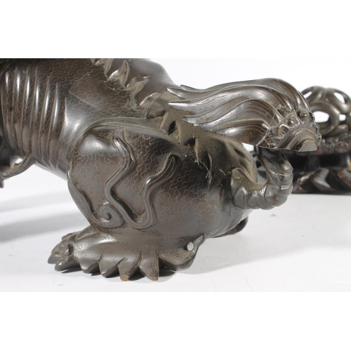 486 - Chinese cast bronze temple dog modelled resting paw on orb, raised on carved wood base, 26cm tall.