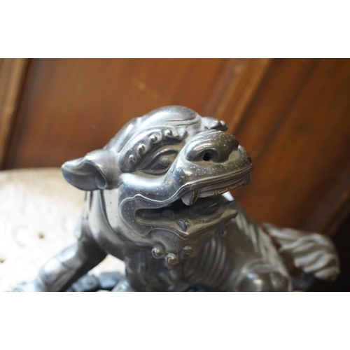 486 - Chinese cast bronze temple dog modelled resting paw on orb, raised on carved wood base, 26cm tall.