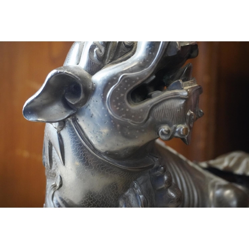 486 - Chinese cast bronze temple dog modelled resting paw on orb, raised on carved wood base, 26cm tall.