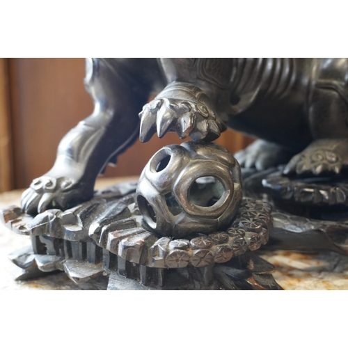 486 - Chinese cast bronze temple dog modelled resting paw on orb, raised on carved wood base, 26cm tall.