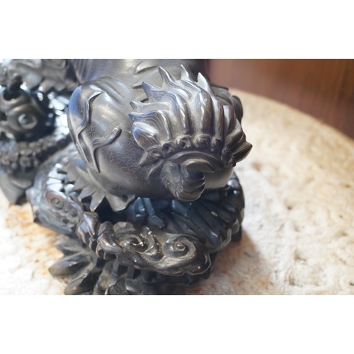 486 - Chinese cast bronze temple dog modelled resting paw on orb, raised on carved wood base, 26cm tall.