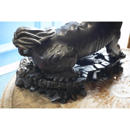 486 - Chinese cast bronze temple dog modelled resting paw on orb, raised on carved wood base, 26cm tall.