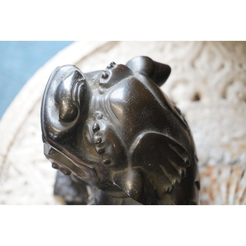 486 - Chinese cast bronze temple dog modelled resting paw on orb, raised on carved wood base, 26cm tall.