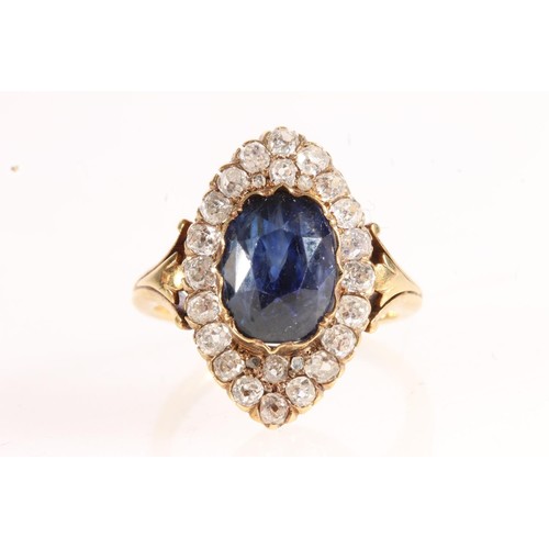 176 - Unmarked yellow metal ring, the large faceted oval sapphire surround by round cut diamonds in a nave... 