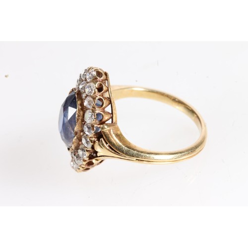 176 - Unmarked yellow metal ring, the large faceted oval sapphire surround by round cut diamonds in a nave... 