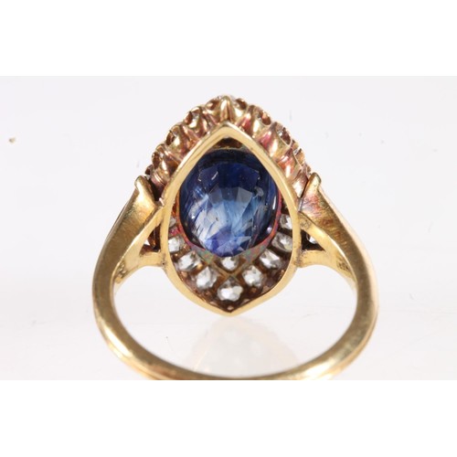 176 - Unmarked yellow metal ring, the large faceted oval sapphire surround by round cut diamonds in a nave... 