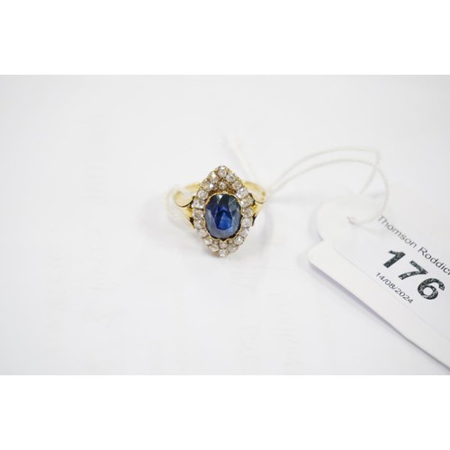 176 - Unmarked yellow metal ring, the large faceted oval sapphire surround by round cut diamonds in a nave... 