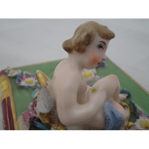 205 - Continental ceramic desk stand with winged putti surmount and integral inkwells, decorated with encr... 