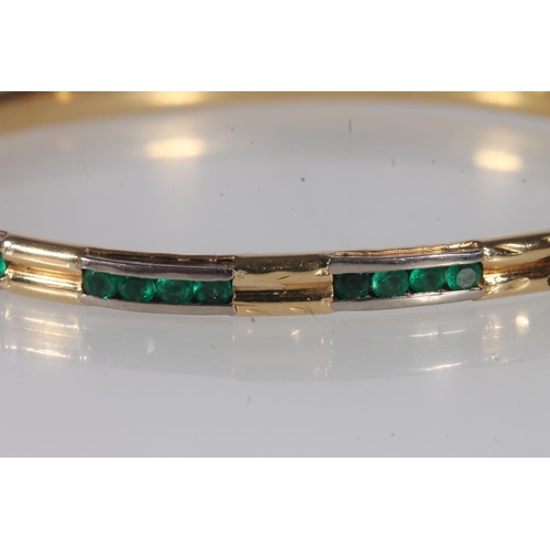 218 - Unmarked yellow gold bangle, on hinged clasp, the face interspersed with channel set round emeralds,... 