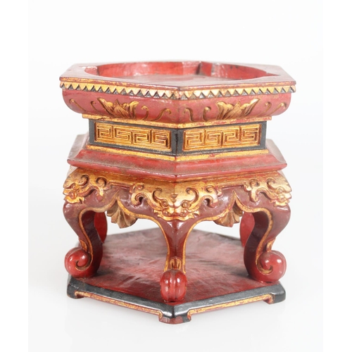 602 - Black red and gilt hexagonal stand with carved detail, raised on six scroll supports and a wooden pl... 