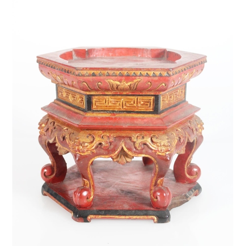 602 - Black red and gilt hexagonal stand with carved detail, raised on six scroll supports and a wooden pl... 