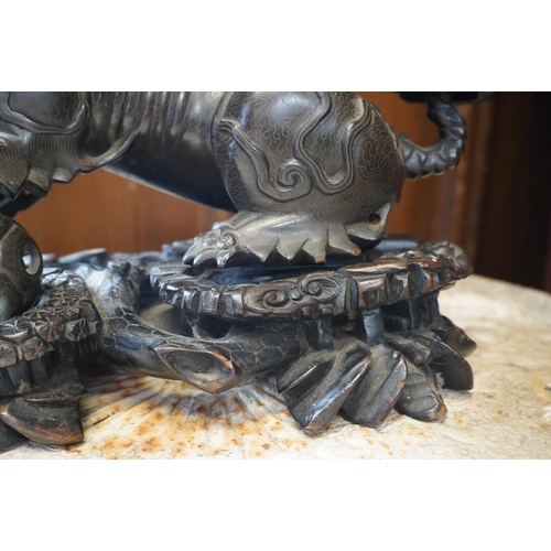 523 - Chinese cast bronze temple dog modelled resting paw on orb, raised on carved wood base, 26cm tall.Do... 